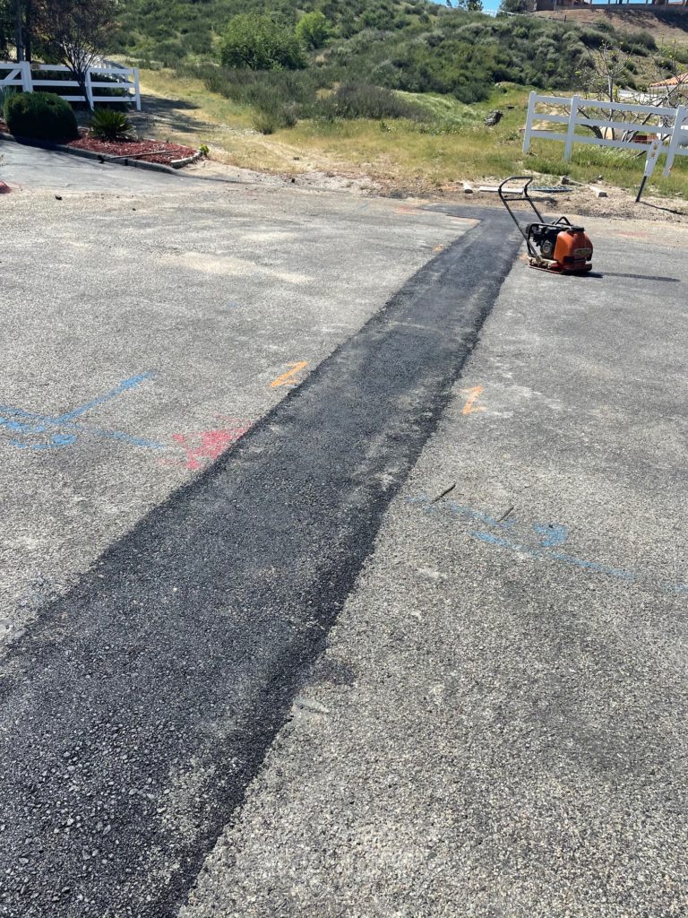 A freshly paved strip of asphalt on an asphalt driveway